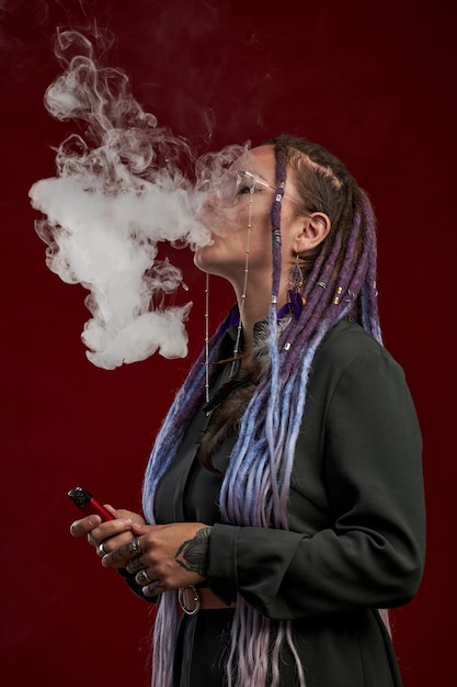 Fille avec des dreadlocks libérant un nuage de fumée tout en tenant un stylo vape