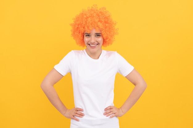 Fille drôle et gaie avec un look fantaisie portant une perruque de cheveux orange sur fond jaune, plaisir de la fête.