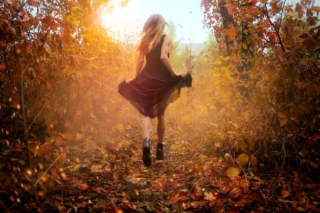 Photo fille drôle en robe noire en cours d'exécution dans la forêt d'automne d'or à l'extérieur