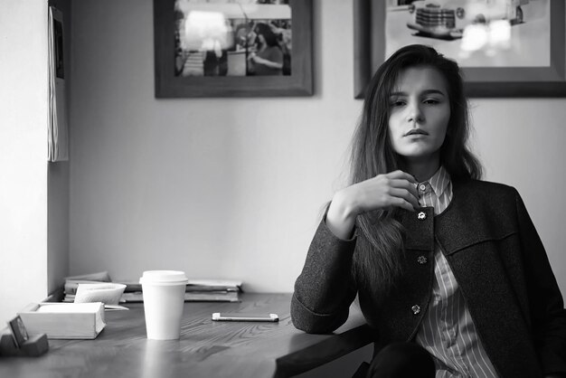 Fille avec du café. Belle jeune fille est assise dans un café et boit du café dans une tasse en papier. La fille prend le petit déjeuner dans le café.