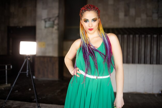 Une fille avec du maquillage et des tresses africaines multicolores dans une robe verte