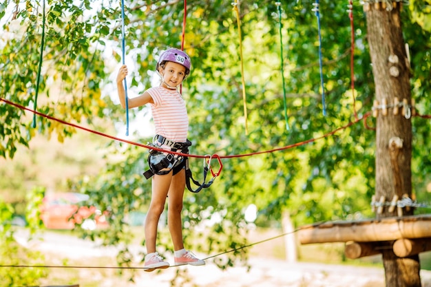 Une fille avec du matériel d'escalade dans un parc d'aventure est engagée dans l'escalade ou passe des obstacles sur la route de la corde