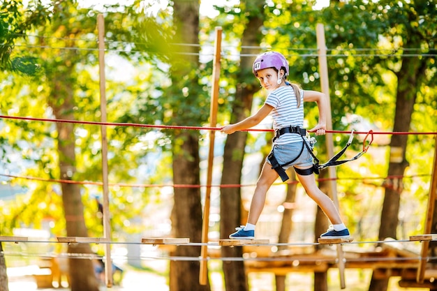 Une fille avec du matériel d'escalade dans un parc d'aventure est engagée dans l'escalade ou passe des obstacles sur la route de la corde