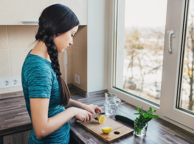 fille du millénaire préparant de l'eau de désintoxication avec du concombre, de la menthe et du citron dans la cuisine de la maison