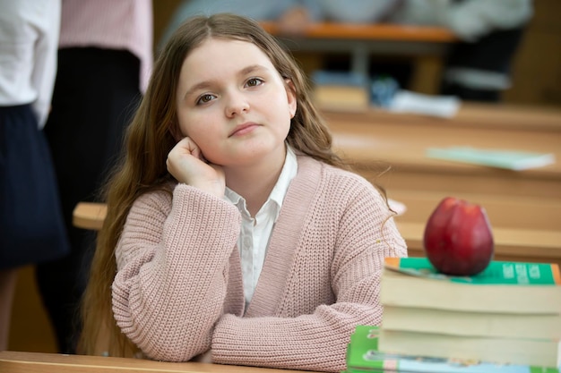 Photo fille écolière au bureau fille dans la salle de classe avec des livres et une pomme