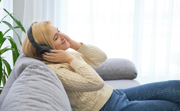 Fille écoutant de la musique avec un casque allongé sur un canapé à la maison