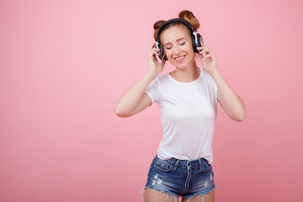 Fille écoute de la musique avec des écouteurs et sourit sur l'espace rose