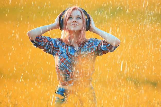 fille avec des écouteurs écoutant de la musique sous la pluie d'été en dehors de la musique d'été