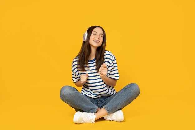 Photo une fille avec des écouteurs écoute de la musique sur un fond jaune