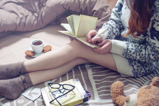 Photo fille écrit dans un cahier assis sur le lit