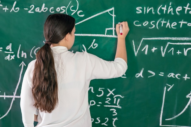 La fille écrit des exemples mathématiques sur le conseil scolaire résout un problème de géométrie