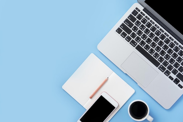 Une fille écrit sur un livre blanc ouvert ou une comptabilité sur un bureau bleu clair minimal et propre avec un ordinateur portable et des accessoires, espace de copie, vue de dessus à plat, maquette