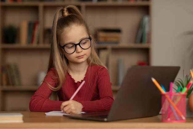 Fille écrivant faire ses devoirs à l'ordinateur portable apprenant à prendre des notes à l'intérieur