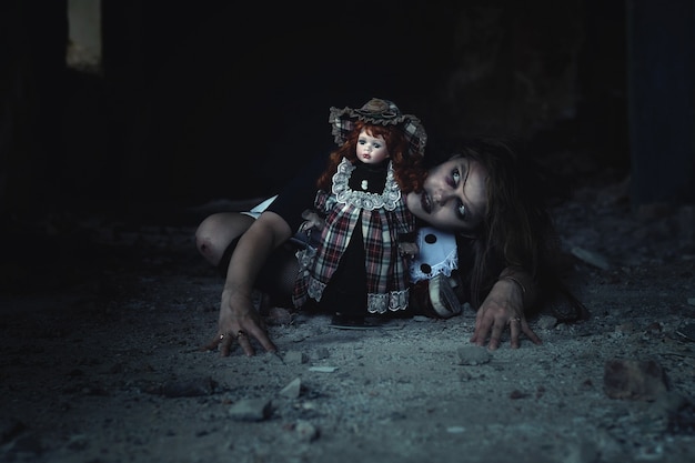 Une fille effrayante avec une poupée sur le sol dans une maison abandonnée. Une idée pour Halloween