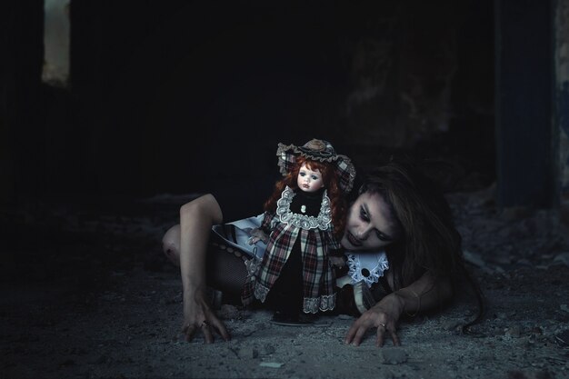 Une fille effrayante avec une poupée sur le sol dans une maison abandonnée. Une idée pour Halloween