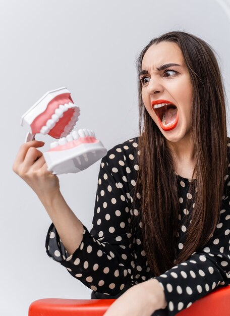 Fille effrayée drôle d'une mâchoire dentaire ouverte près du visage. Femme toing avec modèle de dents éducatives en plastique.