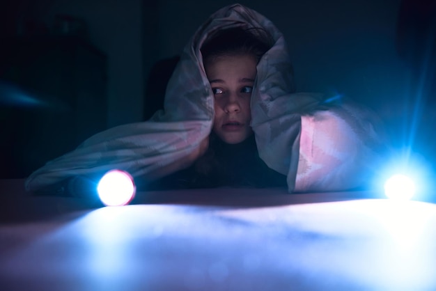 Une fille effrayée avec une lumière se trouvant sous une couverture