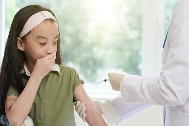Fille effrayée regardant le docteur injectant le vaccin dans son bras