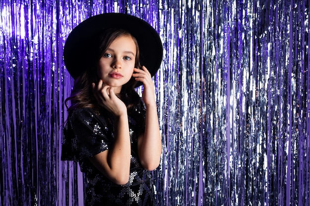 fille élégante avec un chapeau noir à bord sur un clinquant violet