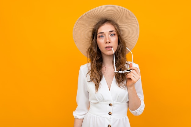 Fille élégante dans un chapeau de paille avec des lunettes de soleil vêtue d'une robe blanche sur fond jaune avec espace copie.