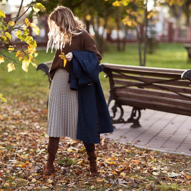 Fille élégante dans un parc en automne dans un pull marron et une jupe à carreaux.