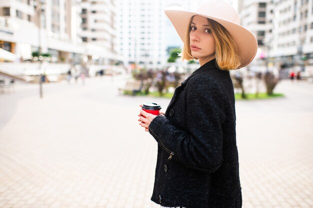 Fille élégante élégante cheveux courts blonde en chapeau posant avec du café sur fond de rue