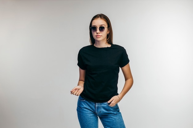 Fille élégante à lunettes portant un t-shirt noir qui pose en studio