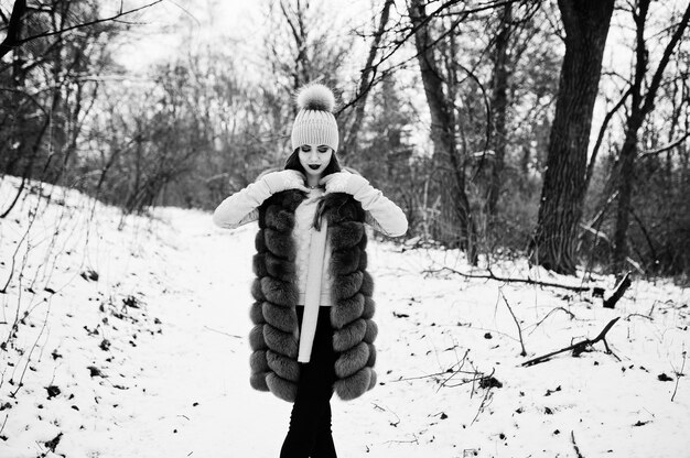 Fille élégante en manteau de fourrure et couvre-chefs à la forêt d'hiver.