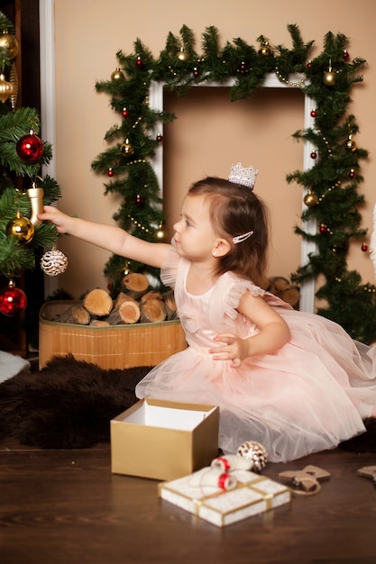 La fille élégante mignonne décore l'arbre de Noël par la cheminée