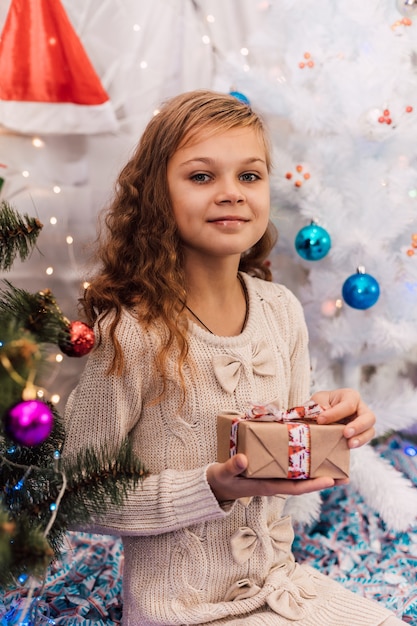 Fille élégante de nouvelle année près d'une épinette décorée verte tenant des cadeaux