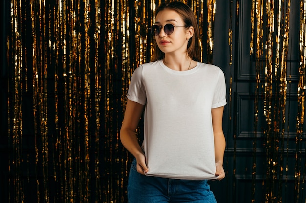 Photo fille élégante portant un t-shirt blanc et des lunettes de soleil posant en studio