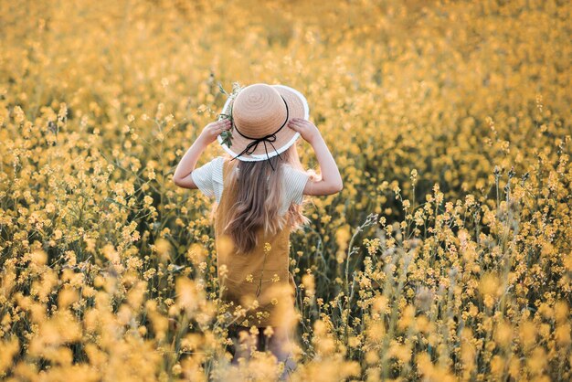 Une fille élégante porte un chapeau de paille et une robe moderne debout dans un pré fleuri en fleurs