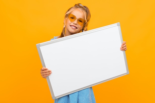 fille élégante tenant un tableau blanc sur un mur jaune