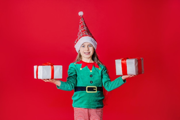 Fille elfe avec des cadeaux Aide du Père Noël sur un fond de couleur vive rouge vif Copiez l'espace