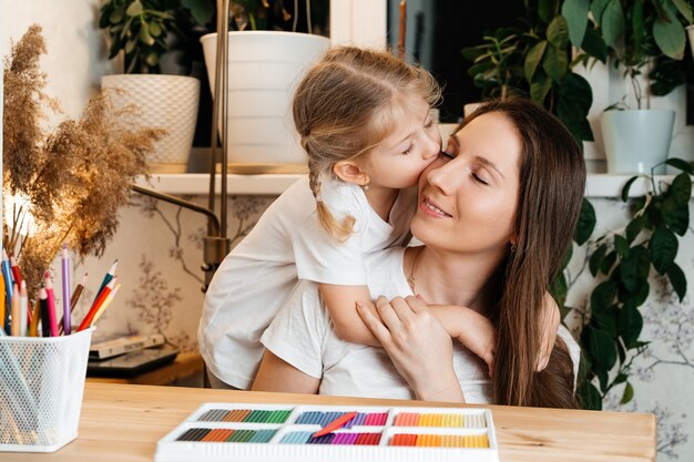 La fille embrasse et embrasse sa mère, ils s'assoient à la table sur laquelle il y a de la pâte à modeler colorée