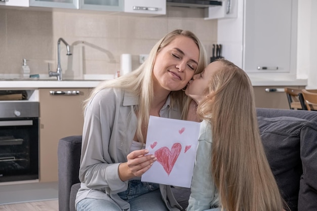 Fille embrasse sa mère dans la joue et donne l'anniversaire carte postale faite à la main mère joyeux anniversaire amour