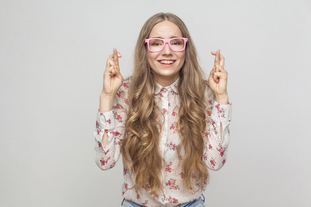 Fille émotive montrant la bonne chance signe ses doigts regardant la caméra et souriant à pleines dents