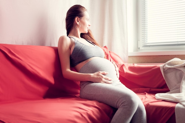 Fille enceinte assise sur un lit et se tient le ventre avec un espace de copie sur un fond