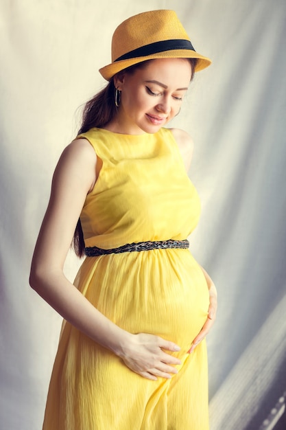 Fille enceinte habillée en robe jaune et chapeau, se tient le ventre