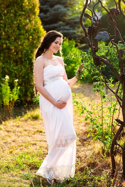 Une fille enceinte heureuse en robe blanche se promène dans le parc.