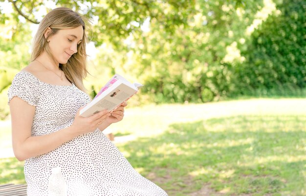 Photo fille enceinte lisant un livre dans le parc