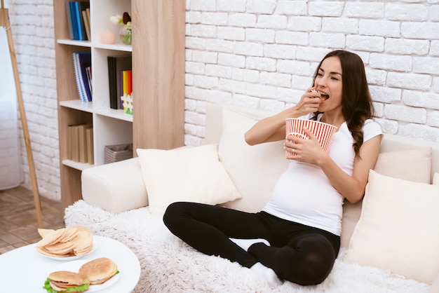 Une Fille Enceinte Mange Beaucoup De Pop-corn Sur Le Canapé.