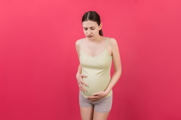 Une fille enceinte qui a mal au ventre se tient sur un fond coloré isolé