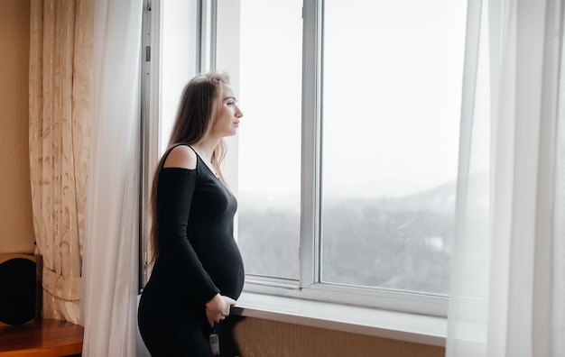 Une fille enceinte respire de l'air frais par la fenêtre.