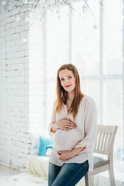 Une fille enceinte rousse dans un chemisier léger et un jean bleu