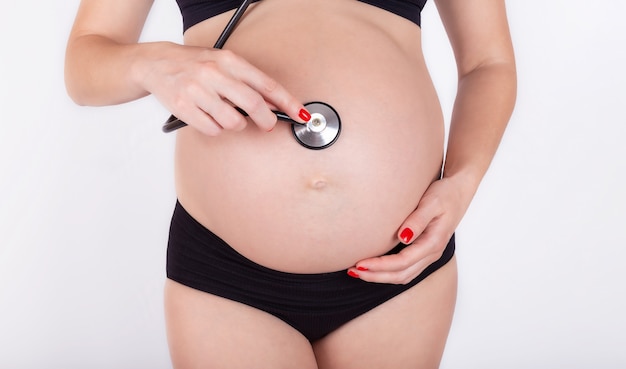 Une fille enceinte avec un stéthoscope écoutant son estomac avec un bébé