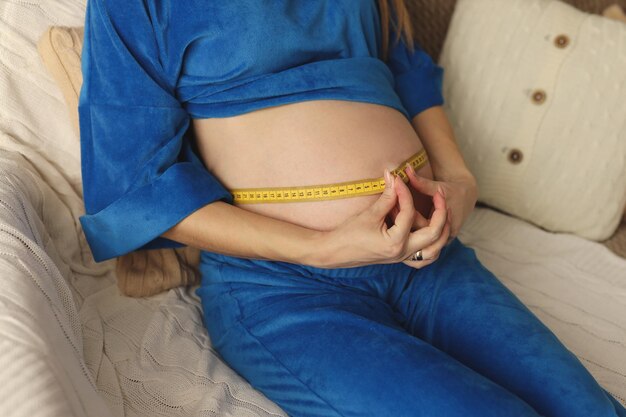 Une fille enceinte vêtue d'un costume bleu vif mesure son ventre avec un mètre ruban