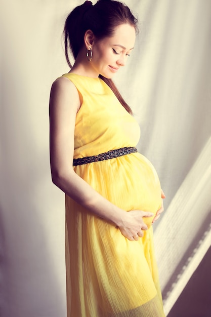 Fille enceinte vêtue d'une robe jaune, se tient le ventre