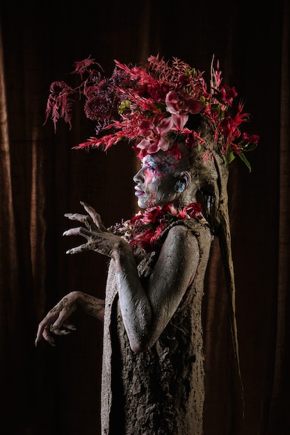 Une fille enduite d'argile dans une robe cimentée. Le modèle a une coiffe en fleurs.