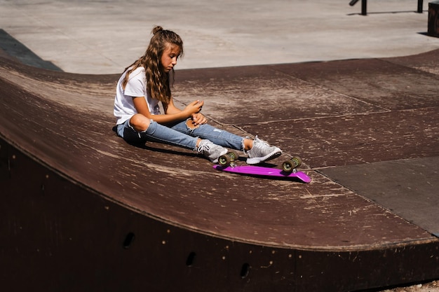 Fille enfant active après la chute d'un penny board blessée assise et ressentant de la douleur sur la rampe de sport sur l'aire de jeux du skate park